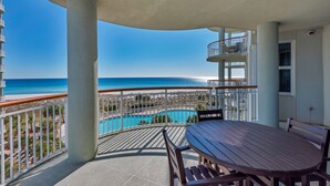 A balcony with a view of the beach and ocean, a pool, and a table with chairs. - Beach Colony West 4A- Gulf-front 3 BD/3BA w/Beach Service & Sleeps up to 8 (Navarre Beach)