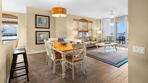 A spacious living area with a dining table, sofa, and a view of the ocean. - Beach Colony West 4A- Gulf-front 3 BD/3BA w/Beach Service & Sleeps up to 8 (Navarre Beach)