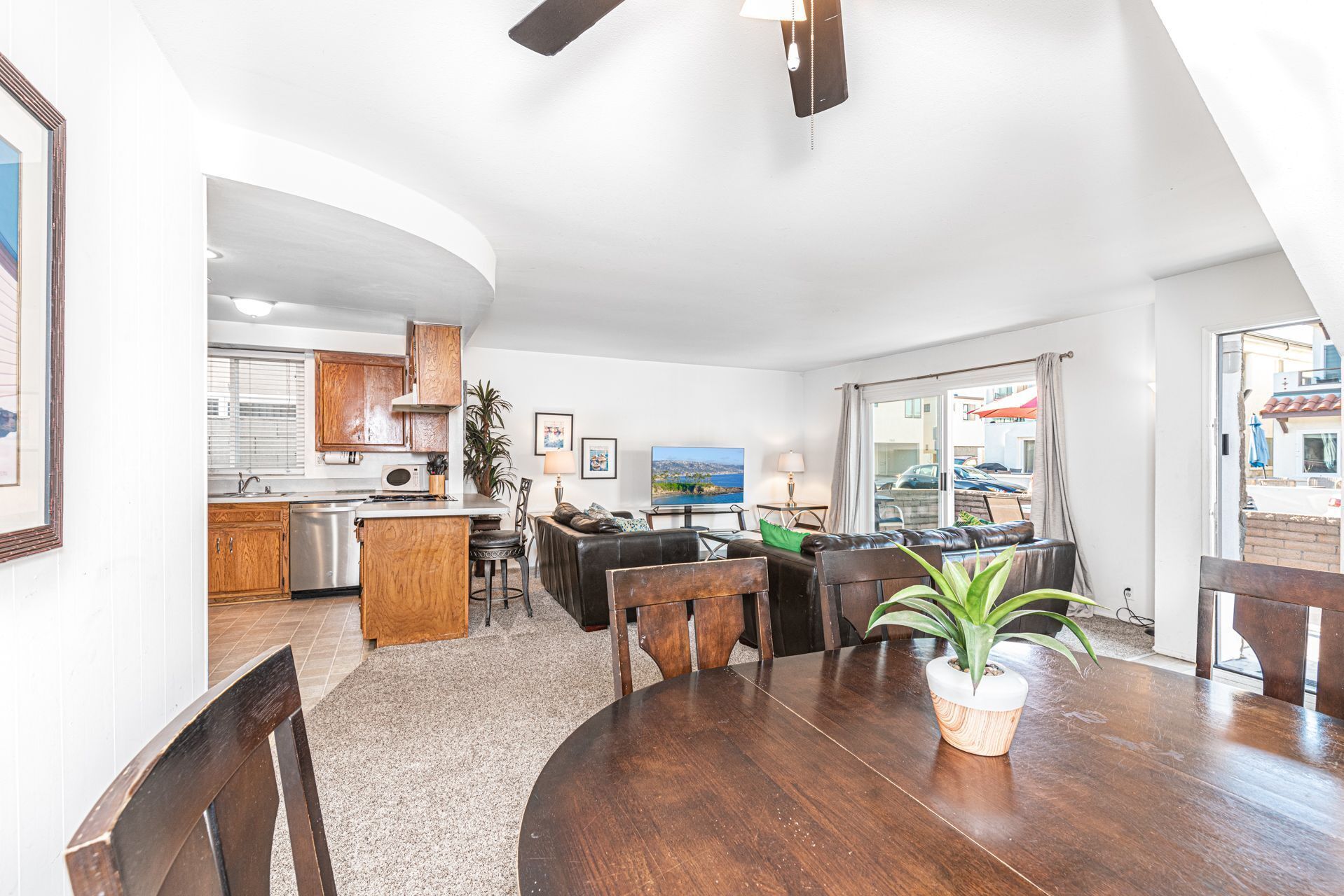 A modern kitchen with wooden cabinets, a dining area with a round table and chairs, and a view of the sea through large windows.