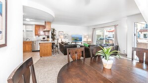 Een moderne keuken met houten kasten, een eethoek met een ronde tafel en stoelen, en uitzicht op zee door grote ramen.