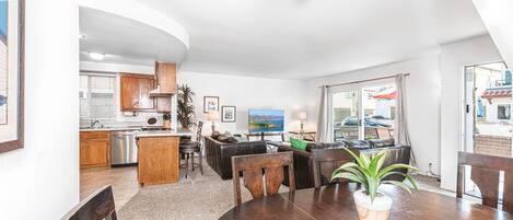 A modern kitchen with wooden cabinets, a dining area with a round table and chairs, and a view of the sea through large windows.