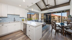 A modern kitchen with white cabinetry, a large island, and a dining area with wooden furniture. - ❤️ Stunning Reno| Amazing Ocean View 💦❤️ (Lahaina-Kaanapali)