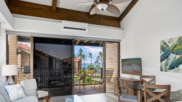 A modern living room with a glass door leading to a balcony with a view of palm trees and the ocean. - ❤️ Stunning Reno| Amazing Ocean View 💦❤️ (Lahaina-Kaanapali)