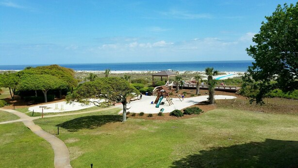 Un parque con un área de juegos, una zona de arena y vistas a la playa y al océano.