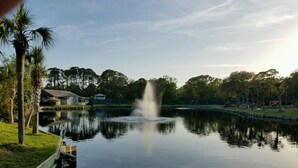 Un lago tranquilo con una fuente en el centro, rodeado de árboles y un muelle.