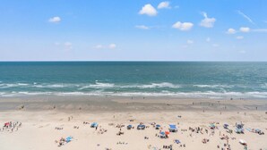 A beach with people sunbathing and swimming, a clear sky, and the ocean. - Beach Chic Oceanfront Condo, Jacuzzi Tub, Lazy River | Crescent Shores - N 1203 (North Myrtle Beach)