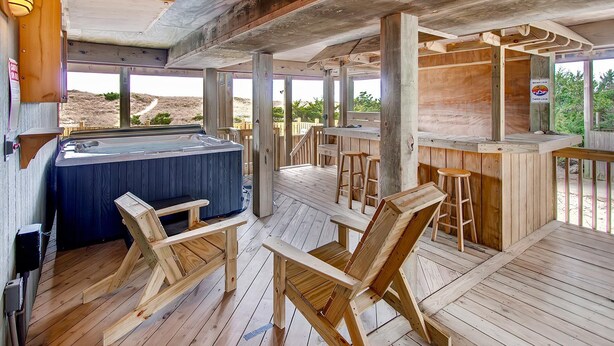 A wooden deck with a hot tub, bar area, and wooden chairs. - Oceanfront Home in Avon with Private Saltwater Pool, Hot Tub, and Tiki Bar (Avon)