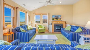 A spacious living room with striped blue sofas, a green armchair, and a fireplace. - Oceanfront Home in Avon with Private Saltwater Pool, Hot Tub, and Tiki Bar (Avon)