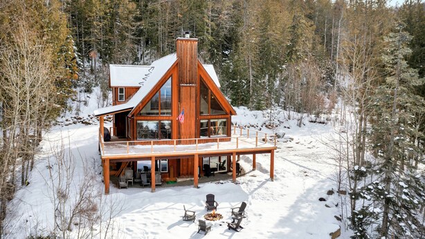 Een chalet met een ruim terras en een open haard, omgeven door sneeuw en bomen.