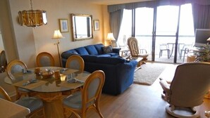 Un salon avec un canapé bleu, une table à manger avec des chaises et une grande fenêtre avec des rideaux.