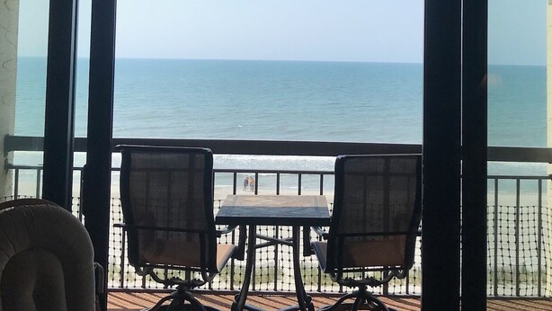Un espace extérieur abrité, avec deux chaises et une table, offrant une vue sur la plage et l’océan.