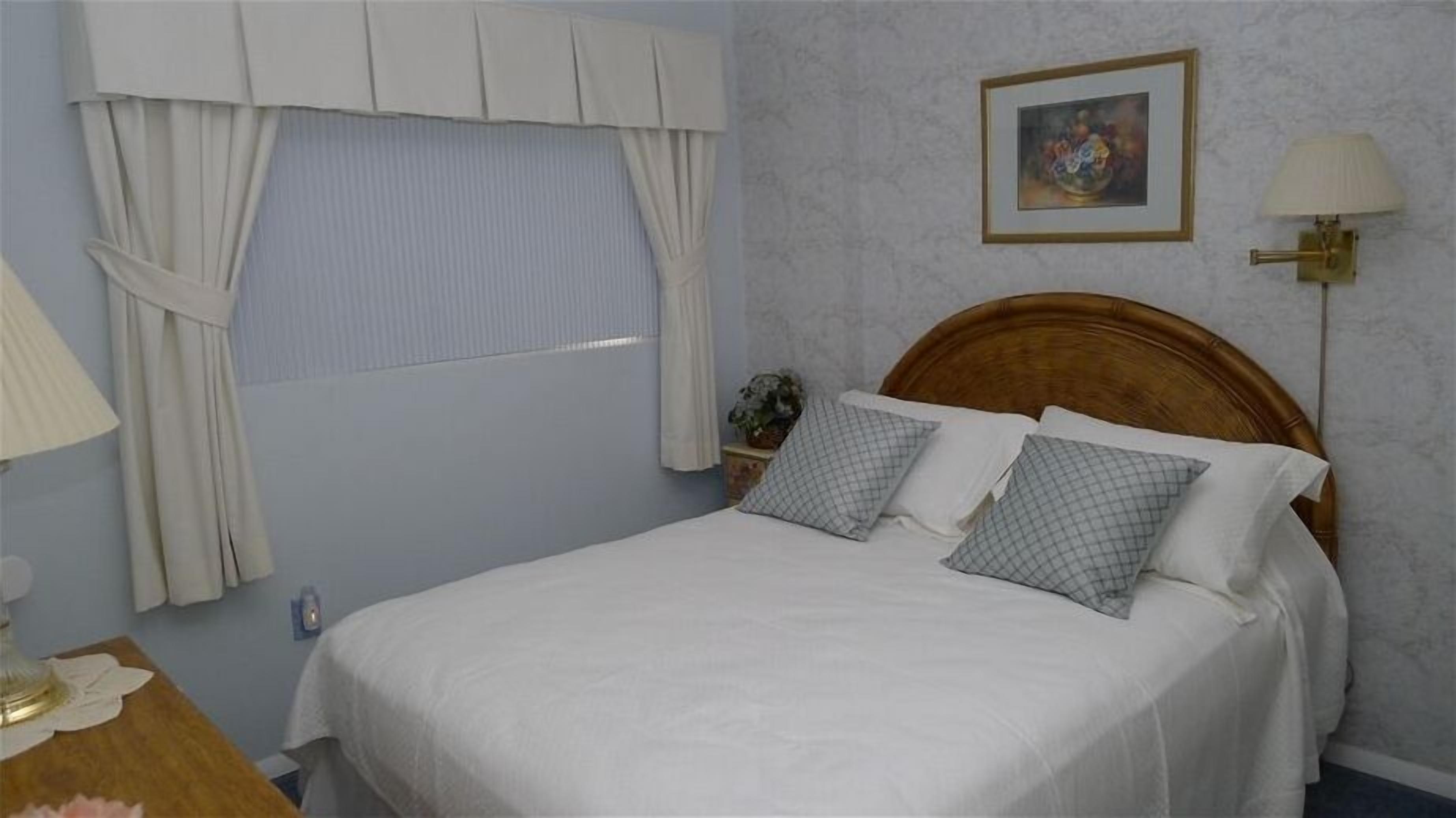 A neatly made bed with a wooden headboard, a bedside table with a lamp, and a window with curtains.