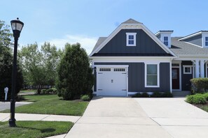 Une maison moderne à deux étages, dotée d’une façade sombre, d’une porte de garage blanche et d’un jardin bien entretenu, avec un trottoir et un lampadaire.
