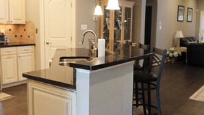 A modern kitchen with a central island, white cabinetry, and a dining area with a black chair. - Upscale Beach & Golf Getaway At Bayside Resort (Selbyville)