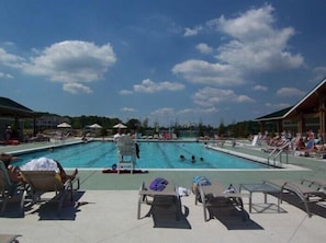 Un espace piscine doté de chaises longues et de parasols, entouré d’immeubles.