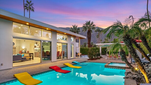 Una casa moderna con piscina, mobiliario exterior y palmeras.