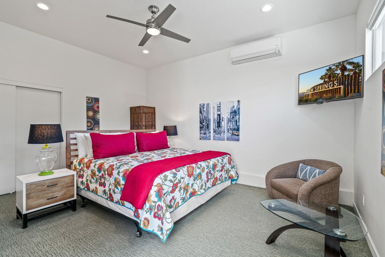 A bedroom with a bed, a chair, a nightstand, a lamp, a ceiling fan, and wall art.