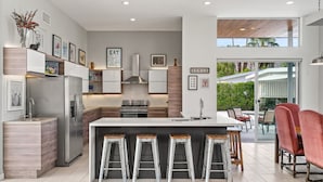 Una cocina moderna con una isla central, electrodomésticos de acero inoxidable y una zona de comedor con sillas rojas.