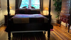 A four-poster bed with a quilt, a ceiling fan, a dresser, and a window with curtains.