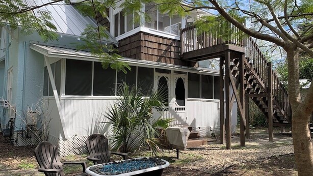 A house with a covered porch, a wooden staircase, and a large window overlooking the yard.
