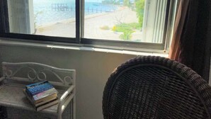 A room with a view of a beach and pier through a window. There is a wicker chair and a small table with a book on it. - Oceanview Retreat Pool Steps Away From Beach U14 (Marathon)