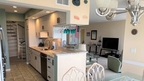 Cocina compacta con comedor, televisor y una escalera que sube a otro nivel.