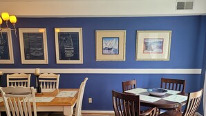 A dining area with a blue wall, wooden dining table, white chairs, and red cushions.