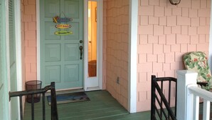 A porch with a green door, a welcome sign, and a bench.