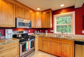 A kitchen with wooden cabinets, a stainless steel stove, a microwave, and a window with a view of greenery. - Lakehouse Getaway For Fun In The Sun (Mount Vernon)
