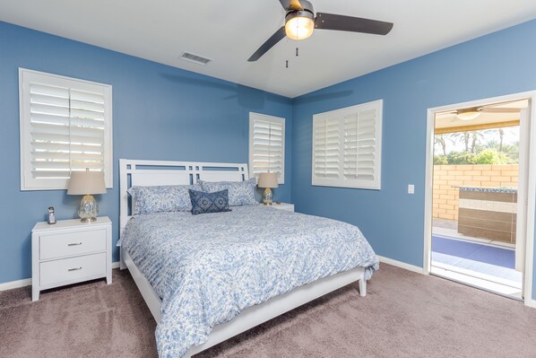 A bedroom with a bed, two nightstands, a ceiling fan, and a view of the outside.