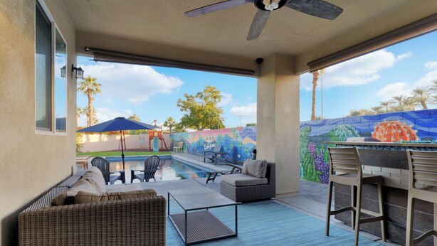 A covered patio with outdoor furniture, a pool, and a mural on the wall. - Family Oasis on 1/4 acre! Pool, putting green + swingset! 30 min to Joshua Tree! (Indio)