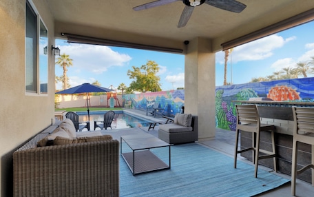 A covered patio with outdoor furniture, a pool, and a mural on the wall.