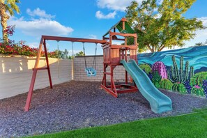 A playground with a swing set and a slide, surrounded by a wall with a cactus mural.