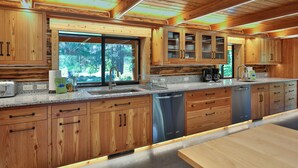 A modern kitchen with wooden cabinets, stainless steel appliances, and a large window offering a view of the outdoors. - Heaven Can Wait Lodge ~ Riverfront Estate on 12 Private Acres ~ Expansive Views (Leavenworth)