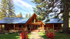 A log cabin with a stone pathway leading to the entrance, surrounded by lush greenery and tall trees. - Heaven Can Wait Lodge ~ Riverfront Estate on 12 Private Acres ~ Expansive Views (Leavenworth)
