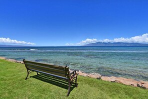 Un banc au bord d’une mer d’un bleu limpide, avec une chaîne de montagnes qui se dessine à l’horizon.