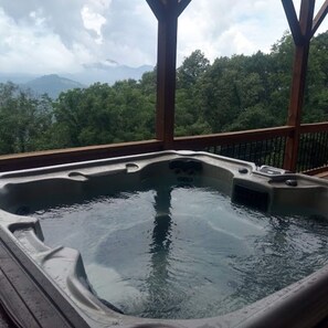 Relax in a hot tub on a spacious outdoor deck with a view of the surrounding landscape.