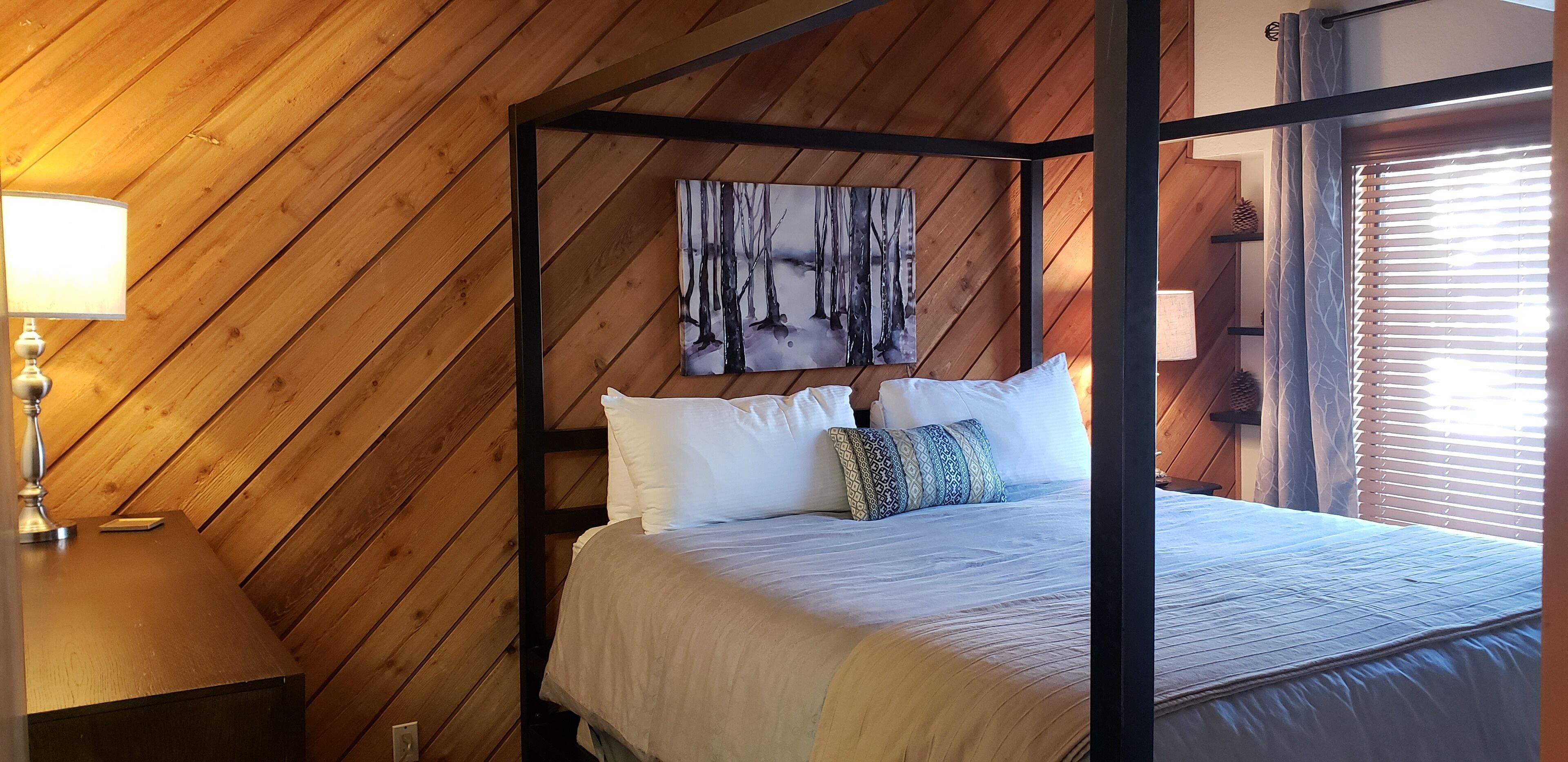 A wooden-paneled room with a four-poster bed, a painting on the wall, and a window with blinds.