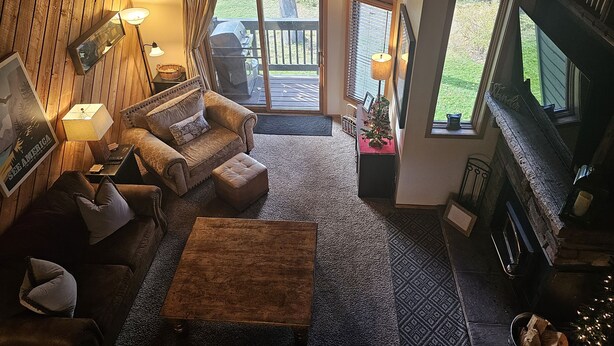Un salon chaleureux avec une cheminée, des murs en bois et une grande fenêtre donnant sur une terrasse.