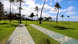 A shuffleboard court with numbers 7, 8, 10, and 10 OFF visible, surrounded by palm trees and a building in the background. - Beautiful, Ocean Front Condo With An Ocean View In Sunny Kihei, Maui! (Kihei)