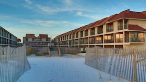 Un hotel con diversi piani, balconi e una zona a terra sabbiosa.