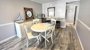 Una cucina compatta con un tavolo rotondo e sedie bianche, una ventola a soffitto e un modellino di una piccola barca a vela.