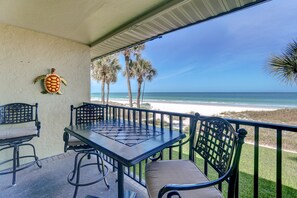 Un espace extérieur abrité, avec une table et des chaises, donnant sur une plage bordée de palmiers et sur l’océan.