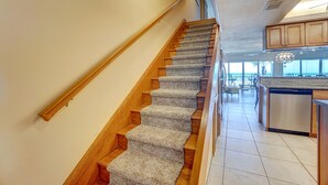A staircase with wooden steps and carpeted risers leading to a kitchen area with wooden cabinets and a dishwasher. - BEAUTIFUL CONDO WITH PERFECT VIEW OF BEACH AND GULF WITH NEW HEATED POOL (Indian Rocks Beach)