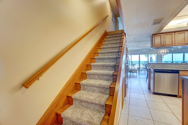 Un escalier avec des marches en bois et des contremarches recouvertes de moquette, menant à une cuisine équipée de meubles en bois et d’un lave-vaisselle.