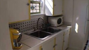 A compact kitchen with white cabinets, a sink, and a microwave. - DOWNTOWN COZY APARTMENT (St Augustine)