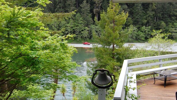 A wooden deck with a bench and a view of a lake surrounded by trees.