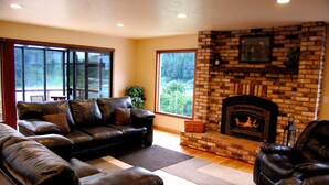 A living room with a brick fireplace, leather sofas, and large windows.