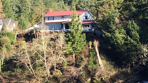 A house with a red roof on a cliff by a lake.
