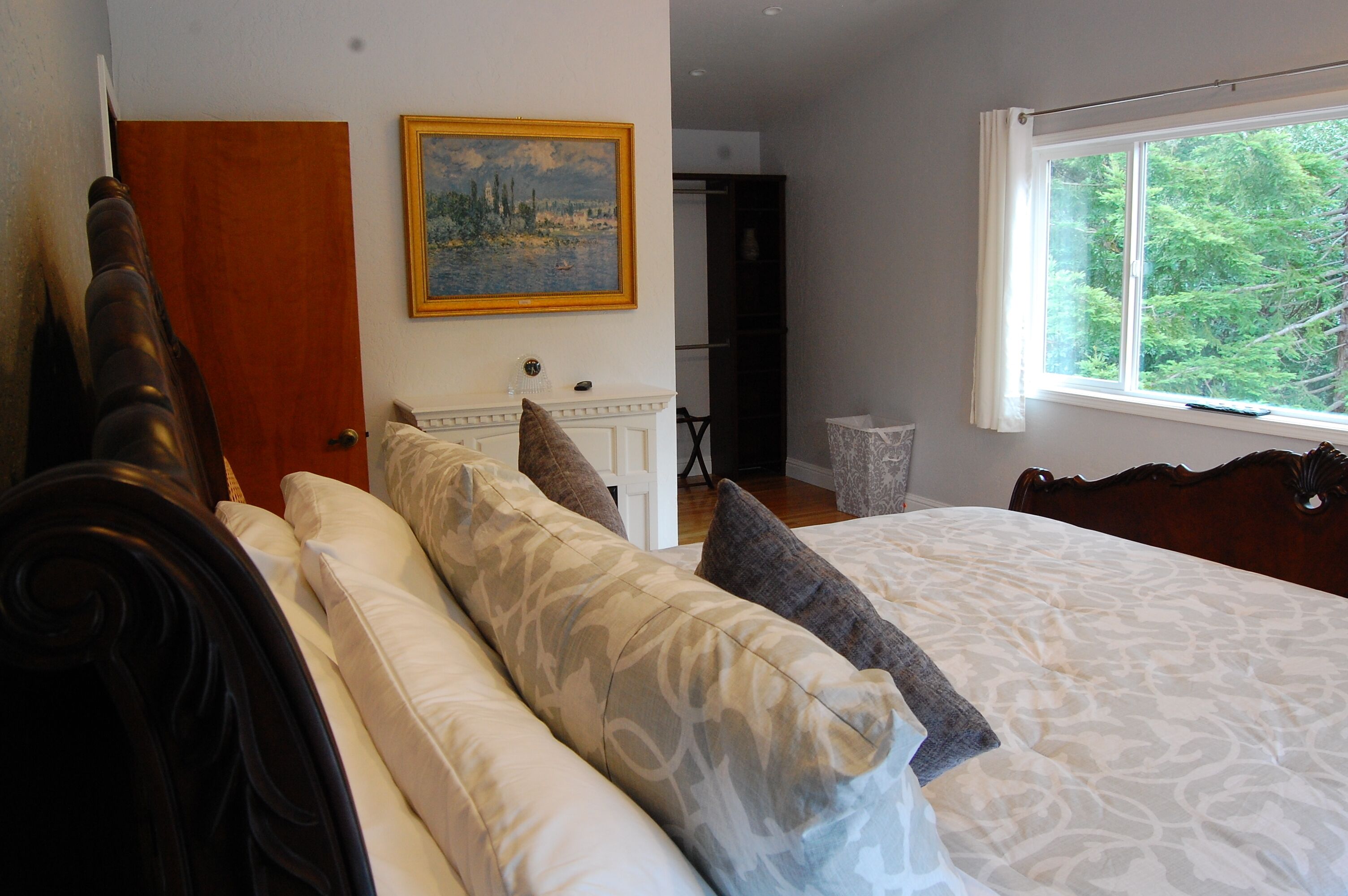 A bedroom with a large bed, a painting on the wall, and a window with a view of trees.